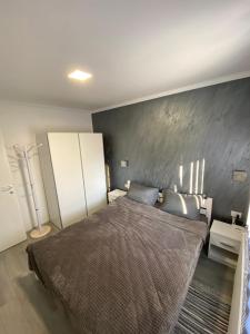 - une chambre avec un grand lit et un mur gris dans l'établissement Apartmani Mira, à Palić