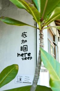 a sign on a wall with a plant in front of it at Here Sleep Guesthouse in Kaohsiung