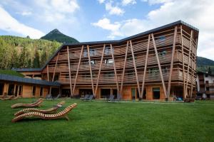 a large building with two wooden benches in the grass at Au Charmant Petit Lac - Ecohotel Parc & Spa in Champoluc