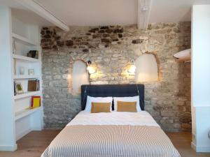 Bett in einem Zimmer mit einer Steinmauer in der Unterkunft La Maison près de la Fontaine in Saignon