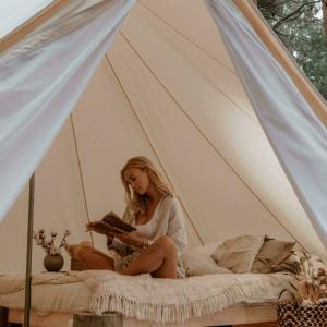 a woman sitting on a bed reading a book at Pop-up glamping - Buurvrouws' Belltentje 2-4 pers in Zuna