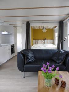 a living room with a black couch and a bed at Tiny house Appelvinkje, huisje met bedstee in bosrijke omgeving in Oisterwijk