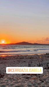 un cartel en la playa con la puesta de sol en el fondo en Hostal Cerro Azul, en Puerto Villamil