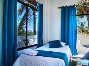 two beds in a room with blue curtains and a window at Hostal Muro De Las Lagrimas with high speed internet Starlink in Puerto Villamil