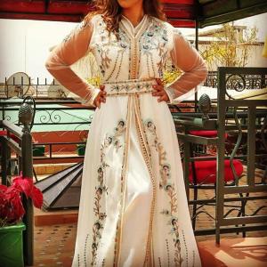 a woman in a white dress standing next to a table at Riad La Porte du Bouregreg in Salé