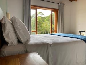 un letto con cuscini bianchi e una finestra in una stanza di Villaggio da Mata a Santo Antônio do Pinhal