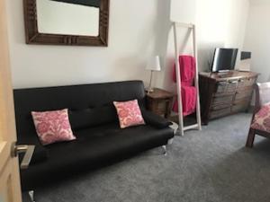 a living room with a black couch and pink pillows at Old Hall cottage in Hope