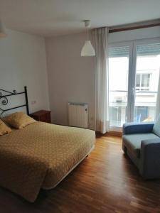 a bedroom with a bed and a couch and a window at Apartamentos MonteBlanco Costa da Morte in Neaño