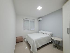 a white bedroom with a bed and a table at Belo Apartamento Eldorado II Master Collection in Passo Fundo