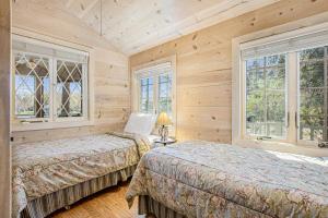 two beds in a bedroom with wooden walls and windows at Anna's Cottage in Saugatuck