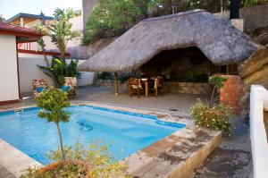 a house with a swimming pool with a thatch roof at Hotel Pension Casa Africana in Windhoek