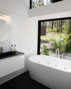 a white bathroom with a large window and a tub at The Bower At Broulee in Broulee