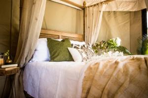 uma cama com lençóis brancos e almofadas verdes em Orchard Valley Glamping em Otorohanga