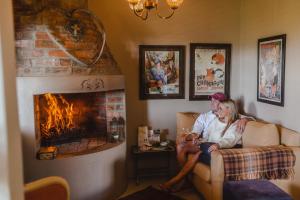 Ein Mann und eine Frau sitzen auf einer Couch vor einem Kamin in der Unterkunft Courchevel Cottages in Franschhoek