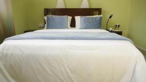 a large bed with white sheets and blue pillows at MAMIKKI Hotel Apartments in Tororo