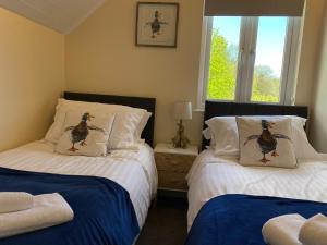 two beds in a bedroom with two ducks pillows at Cotswolds Lakeside Lodge - Nesbitt's Nest in South Cerney