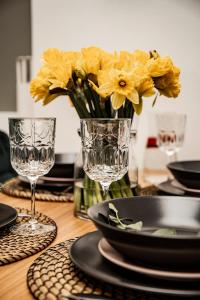 a table with glasses and a vase of yellow flowers at MOOD Apartamenti Kuldīgā in Kuldīga