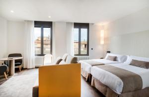 ジローナにあるペニンスラールのベッド2台、テーブルと椅子が備わるホテルルームです。