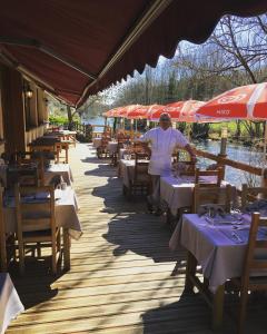 un hombre de pie en un restaurante con mesas y sombrillas en Hotel Restaurant Les Gorges de Chouvigny, en Chouvigny