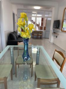un jarrón de flores amarillas sentado en una mesa de cristal en Pingvin Cukrászda Apartman felső szint, en Balatonmáriafürdő