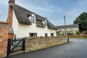 a white house with a thatched roof and a stone wall at Cotswold Thatched Cottage in Mickleton