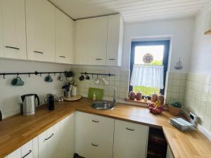 eine Küche mit weißen Schränken, einem Waschbecken und einem Fenster in der Unterkunft Reethaus Niedlich in Middelhagen