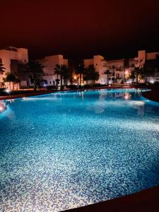 a large blue swimming pool at night with buildings at Appartement perla saidia in Saïdia