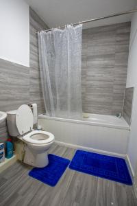 a bathroom with a toilet and a shower with blue rugs at Cherry Tree, Centrally Located Warrington Town Centre in Warrington