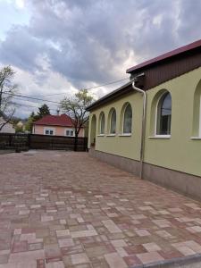 a yellow building with windows and a brick driveway at Halász Vendégház in Szilvásvárad