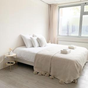 een witte slaapkamer met een bed met witte lakens en een raam bij Sea you soon in Den Burg