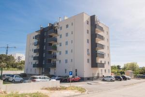 a tall white building with cars parked in a parking lot at Romanca in Zadar