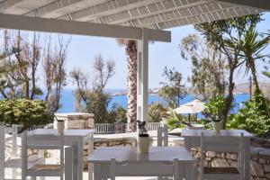 un patio con mesas y sillas blancas y el océano en High Mill Paros Hotel, en Parikia