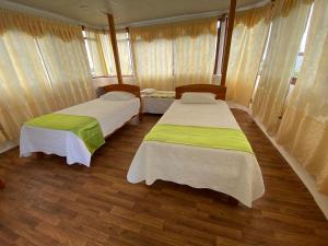 two beds in a room with wooden floors and windows at Hostal Casa Edén in Puerto Ayora