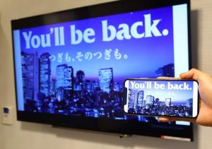 APA Hotel Nagoya Ekimae في ناغويا: شخص يحمل جوال امام التلفزيون