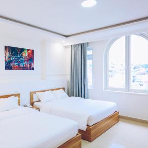 two beds in a white room with a window at TTR An Nam Apart Hotel in Da Lat