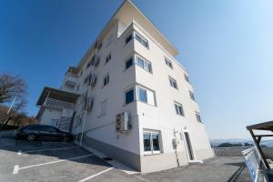 a white building with a car parked in a parking lot at Al Hayat Apartments in Vogošća