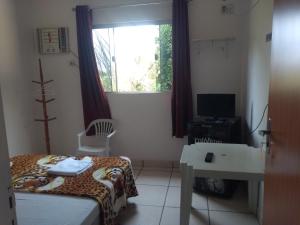 a bedroom with a bed and a desk and a window at Chácara Pousada Sagui in Cuiabá