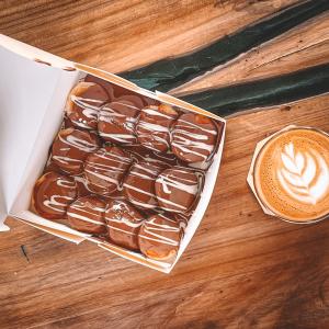a box of chocolate covered donuts and a cup of coffee at Sharz Hotel in Buraydah