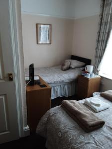 a room with two beds and a desk with a television at Chantry Villa Hotel in Skegness +15 photos