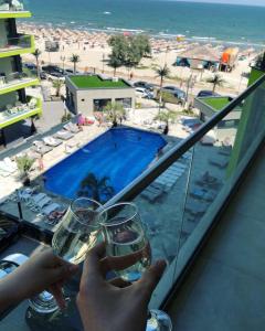 a person holding two glasses of wine in front of a pool at Apartament Rai Alezzi Beach Resort Mamaia Nord in Năvodari