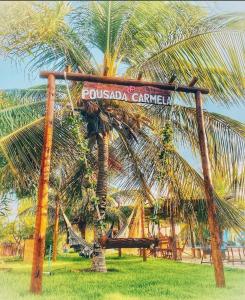 a sign in front of a palm tree with a hammock at Pousada Carmela in Icapuí