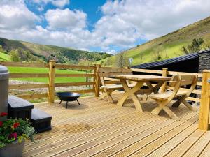 um deque de madeira com uma mesa de madeira e bancos em Mid Wales Luxury Huts em Darowen