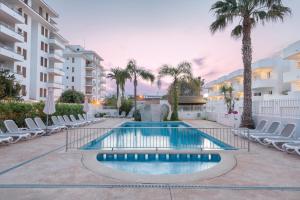a swimming pool with chairs and palm trees at Olive Beach Apartamentos in Port d'Alcudia