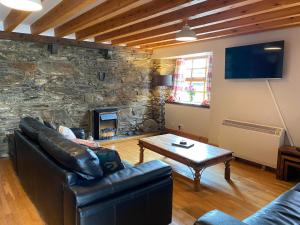 a living room with a leather couch and a stone wall at Mawenyoupe in Lochgilphead