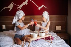 two women sitting on a bed with a table with drinks at Ays Design Hotel Rosa Khutor in Estosadok