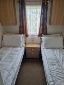 two beds in a small room with a window at 8 BERTH DELUXE CARAVAN Pg156 GOLDEN PALM CHAPEL ST LEONARDS in Chapel Saint Leonards