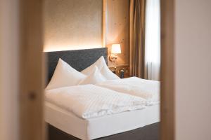 a bed with white sheets and pillows in a room at Hotel Alpenhof in Tirolo