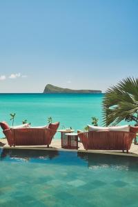 einen Pool mit Stühlen und das Meer im Hintergrund in der Unterkunft Paradise Cove Boutique Hotel (Adults Only) in Cap Malheureux