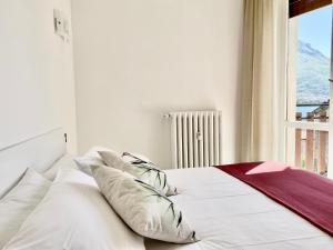 a bed with white sheets and pillows next to a window at Lilla Apartment Vassena in Oliveto Lario