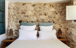 a bed with white pillows in a room with a stone wall at Masseria del Gigante in Carpignano Salentino